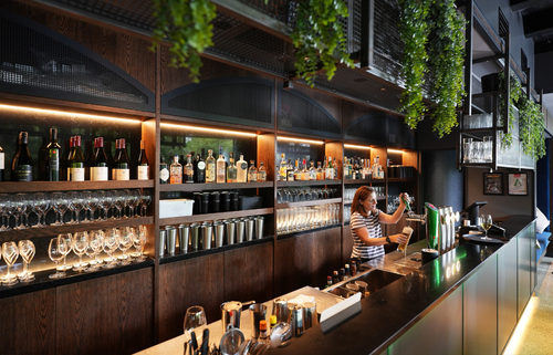 Woman working as a bartender pouring a drink behind a large bar.