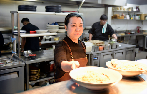 Woman in kitchen at the back of a restaurant putting bowls of food down on the counter