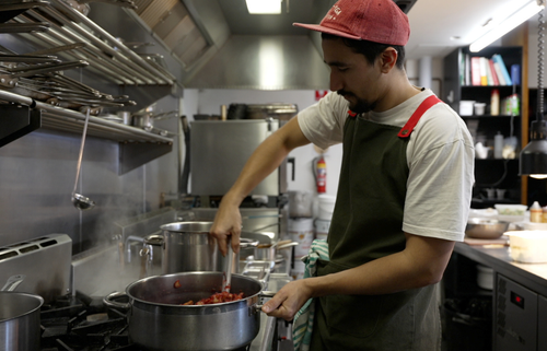 Man in back kitchen at a restaurant stirring food in a pot