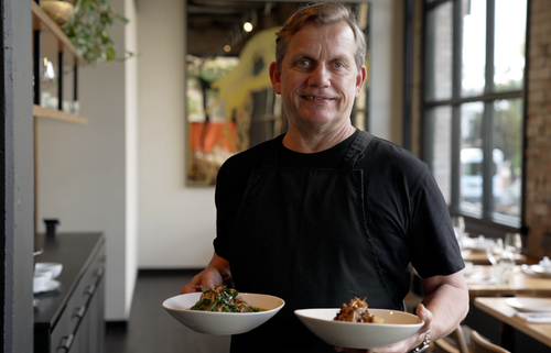 Man holding two bowls of food, one in each hand.